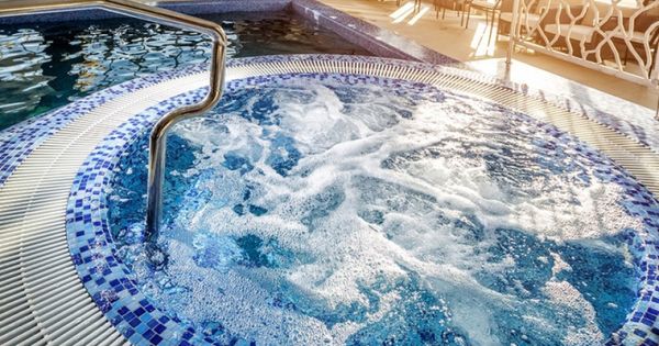 Круглая джакузи с пузырящейся водой, выложенная синей мозаикой, рядом бассейн