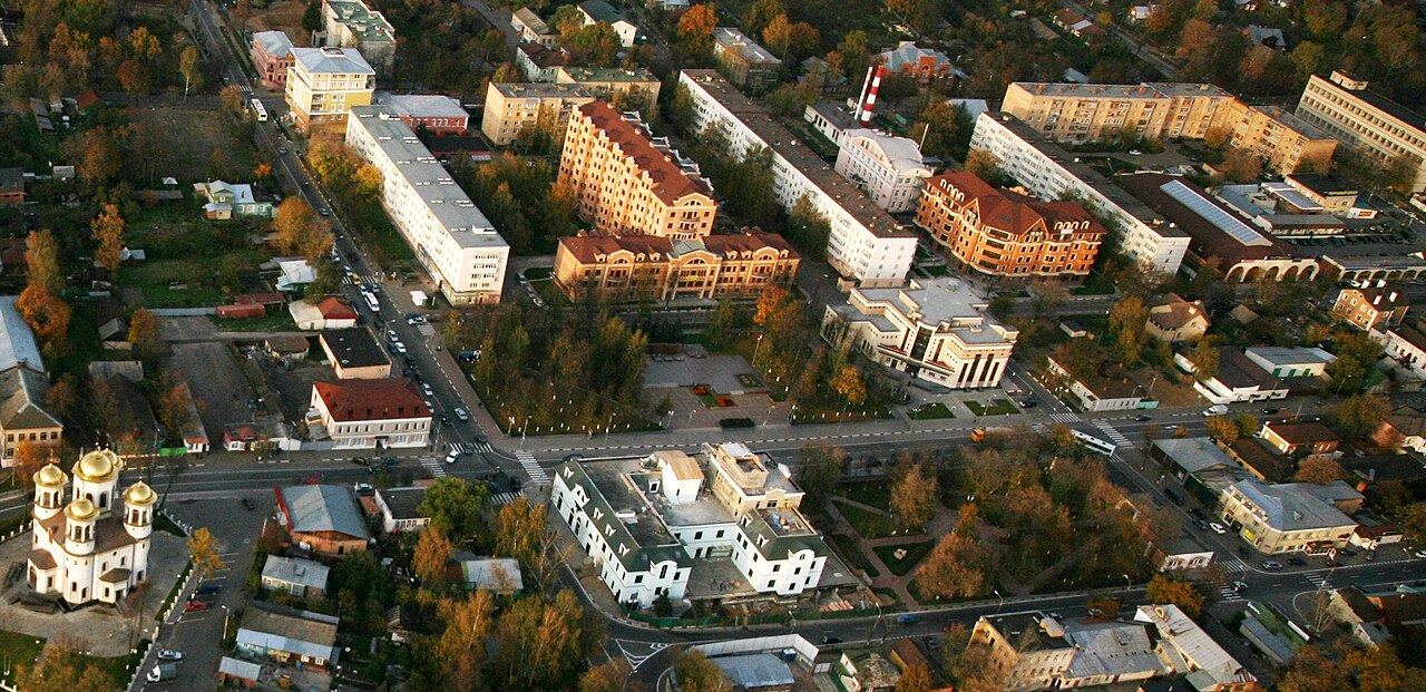 Вид с высоты на центр города осенью: жилые дома, улицы, парк и небольшая церковь с золотыми куполами.